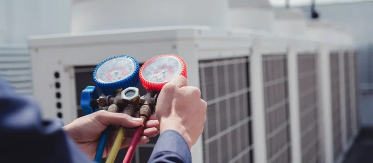 Person using a manifold gauge set to inspect or adjust a rooftop air conditioning unit.