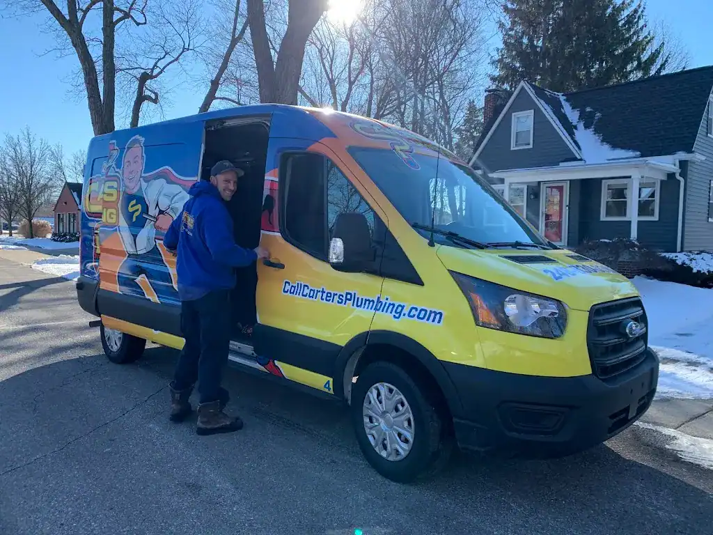 Person standing beside a brightly colored plumbing service van on a suburban street with houses and trees visible in the background.