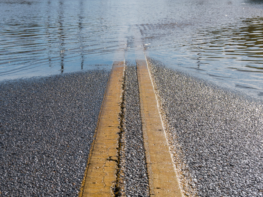 A paved road with yellow center lines disappearing into deep floodwater during the 2026 Michigan flooding crisis.